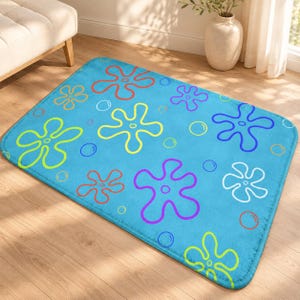 Peut inclure: Un tapis rectangulaire présentant un fond bleu vif avec un motif répétitif de fleurs colorées à cinq pétales dans des tons de rouge, orange, jaune, vert, violet et blanc, parsemé de petits contours circulaires simples.