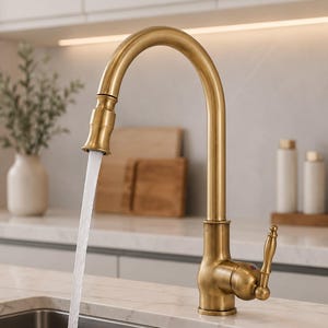 Può includere: Un rubinetto da cucina in ottone spazzolato con bocca alta e una leva laterale singola. L'acqua scorre dalla testina estraibile. Il rubinetto presenta una finitura metallica ed è posizionato sopra un lavello in acciaio inossidabile.