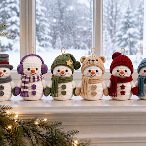 May include: Six crocheted snowman ornaments arranged in a row, each wearing a unique hat and scarf set in colors including gray, purple, green, tan, red, and blue. Each snowman features a white body, orange nose, and two buttons on the front.