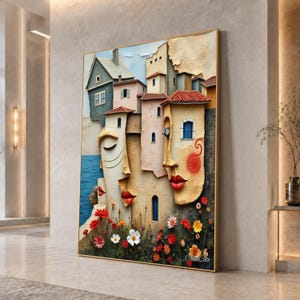 May include: A large rectangular wall art piece featuring a surreal composition where architectural building facades blend into human facial features. The scene includes textured houses, red roofs, blue windows, and vibrant red and white flowers.