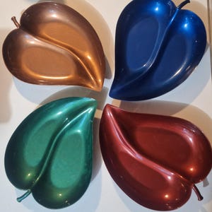May include: A set of four leaf-shaped dishes in metallic finishes. The dishes are colored copper, royal blue, emerald green, and deep red. Each dish features a central vein detail and a small stem at the base, with a smooth, reflective surface.