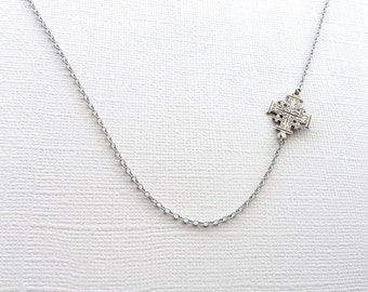 May include: A silver chain necklace with a silver cross pendant. The cross is detailed with intricate designs.