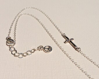 May include: A silver chain necklace with a peace sign charm and a cross pendant.