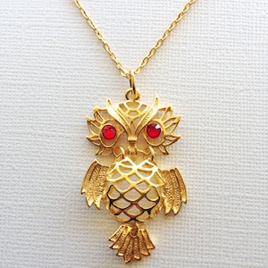 May include: A gold owl pendant necklace with red gemstone eyes. The owl is detailed with a delicate, intricate design.