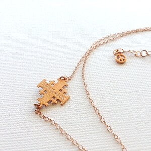 May include: Gold necklace with a Jerusalem cross pendant and a peace sign charm. The cross pendant has the word "Jerusalem" inscribed on it.