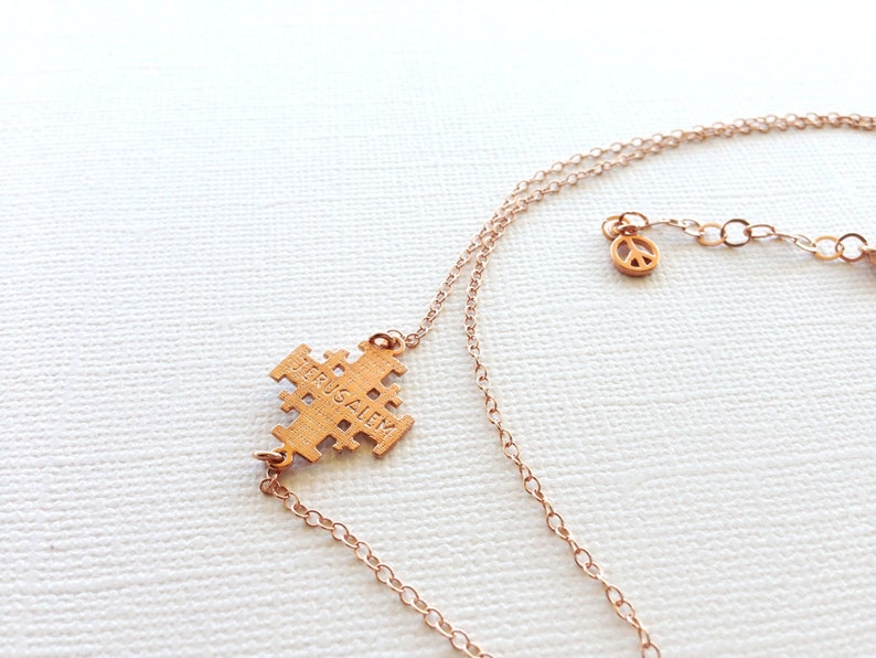 May include: Gold necklace with a Jerusalem cross pendant and a peace sign charm. The cross pendant has the word "Jerusalem" inscribed on it.
