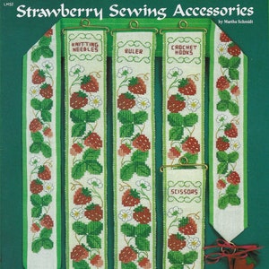 May include: Five white fabric needlepoint bookmarks with a strawberry design. Each bookmark has a different label: Knitting Needles, Ruler, Crochet Hooks, Scissors, and Needles. The bookmarks are hanging from a gold metal rod. The image also includes two small white fabric needlepoint pouches with a strawberry design. One pouch is labeled "Needles".