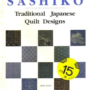 Pode incluir: Um livro intitulado "Sashiko: Desenhos Tradicionais de Colchas Japonesas" de Nihon Vogue. A capa apresenta uma grade de nove quadrados, cada um contendo um padrão de ponto sashiko diferente. Um adesivo de preço amarelo com o texto "15" está na capa.