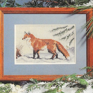 May include: A framed cross-stitch embroidery of a red fox standing in a snowy forest setting. The fox is facing left and has a bushy tail.