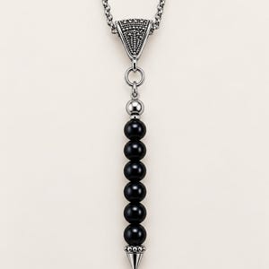 May include: A silver-toned necklace featuring a vertical pendant with six smooth, round black beads. The pendant is suspended from a textured, triangular silver-toned bail and terminates in a pointed silver-toned metal tip at the bottom.
