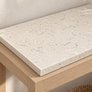 Op de afbeelding: Een rechthoekige sidetable met een frame van licht eikenhout en een gepolijst beige stenen blad met subtiele grijze spikkels. De tafel heeft een onderste plank met een gevlochten mand en een stapel witte stoffen, met een donkere vaas erbovenop.