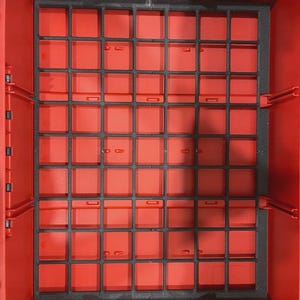 May include: A rectangular red plastic storage bin featuring a black grid insert that creates multiple square compartments. The interior walls of the bin are solid red with vertical structural ribs, and the black grid is positioned flat at the base.
