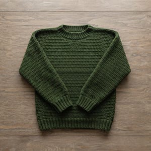 May include: A forest green long-sleeve sweater featuring a textured crochet knit pattern, a round neckline, and ribbed cuffs and hem. The garment is constructed with a consistent horizontal stitch design throughout the body and sleeves.