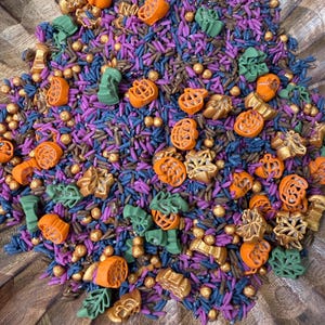 Peut inclure: Un mélange festif de décorations sucrées comprenant des formes de citrouilles orange, des feuilles vertes, des billes métalliques dorées et de petits bâtonnets violets et bleu foncé. Cet assortiment est destiné à décorer les pâtisseries.