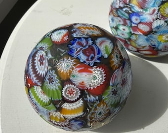May include: Two spherical glass paperweights featuring a millefiori pattern. Each orb is densely packed with multicolored floral-shaped glass canes in shades of red, blue, green, yellow, and white, creating a complex mosaic of intricate glass designs.