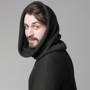 May include: A man wearing a dark green hooded sweater with a ribbed texture. The hood is pulled up over his head, and he is looking over his shoulder.