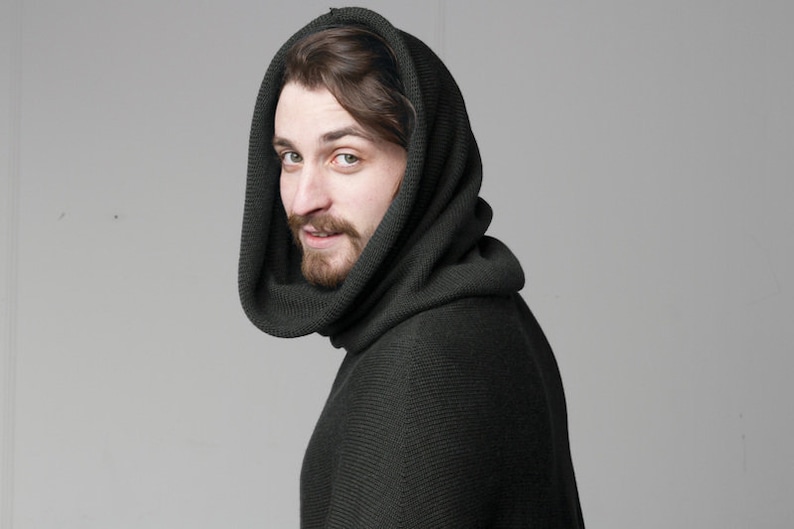 May include: A man wearing a dark green hooded sweater with a ribbed texture. The hood is pulled up over his head, and he is looking over his shoulder.