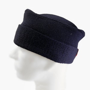 May include: A dark blue wool cap with a red trim. The cap has a unique shape with a pointed top and a curved brim.