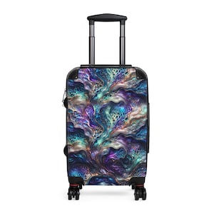 Puede incluir: Una maleta con ruedas que presenta un patrón de arte fluido abstracto y vibrante en tonos morado intenso, azul verdoso y azul. El equipaje rígido tiene un marco negro, un asa plateada retráctil y cuatro ruedas giratorias negras en la base.