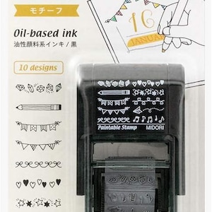 Puede incluir: Un sello negro Midori Paintable Stamp en su embalaje original. El sello cuenta con una rueda giratoria con 10 diseños distintos, incluyendo corazones, estrellas, notas musicales y guirnaldas. El embalaje muestra el texto Paintable Stamp.