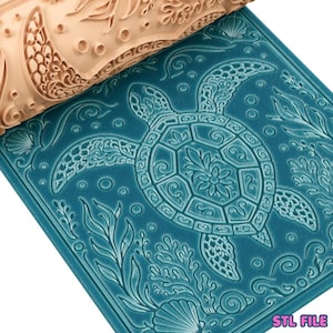 May include: A beige cylindrical rolling pin with a deeply engraved sea turtle and ocean-themed pattern, shown pressing into a flat, teal-colored slab of material to create a raised, detailed impression of a turtle, seaweed, and seashells.
