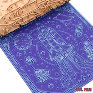 May include: A beige cylindrical rolling pin with a carved space-themed pattern featuring a space shuttle, moon, stars, and a capsule. The rolling pin is positioned above a purple surface embossed with the same detailed space exploration design.