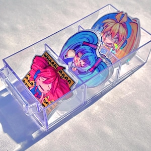 May include: A clear plastic organizer tray containing three distinct anime-style character stickers. One sticker features a pink-haired character with the text "WHAAAA" repeated, another shows a blue-haired character, and the third depicts an orange-haired character.