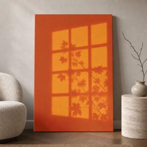 May include: A rectangular canvas print featuring a solid burnt orange background. The artwork displays a projected shadow of a window frame with twelve panes, overlaid with the silhouette of maple tree branches and leaves in a darker orange.
