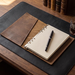 May include: A brown leather binder with a six-ring metal mechanism holding cream-colored paper. The interior flap features an engraved quote: A gentle answer turns away wrath, but a harsh word stirs up anger. Love is patient; love is kind.