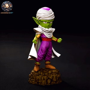 May include: A small green-skinned humanoid figurine with pointed ears, wearing a white turban with a purple top, a white cape, a purple jumpsuit with a red sash, and brown boots. The character stands on a textured brown rock-like base.