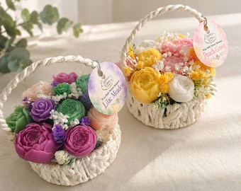 May include: Two small woven baskets with handles, each filled with wax flower shapes. One basket features purple, green, and peach wax flowers with a tag labeled Lilac Meadow. The other contains yellow, pink, and white wax flowers with a Peach Grove tag.