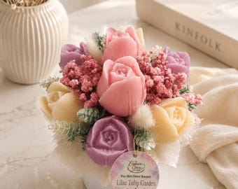 May include: A wax melt flower bouquet in a white container featuring pink, yellow, and purple tulip-shaped wax melts interspersed with dried flowers. A round tag attached to the front reads Essence Cove Wax Melt Flower Bouquet Lilac Tulip Garden.