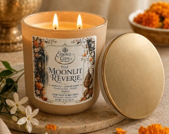 May include: A beige glass candle with two lit wicks and a gold lid. The label reads Essence Cove, The Moonlit Reverie, Marigold, Jasmine Sambac, Ylang Ylang, Honey, Benzoin, Luxury Olive Oil Wax Candle, Net Wt. 10 oz (283 g).