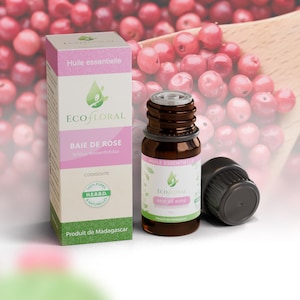 Peut inclure: Un flacon d'huile essentielle en verre brun et sa boîte en carton assortie, tous deux étiquetés EcoFloral Baie de Rose. L'emballage présente des accents roses et verts, du texte en français et un logo feuille verte. Bouchon noir à vis.