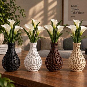 Può includere: Quattro vasi in nero, bianco, marrone e beige, ciascuno caratterizzato da un guscio esterno cavo, organico e simile a un reticolo. Ogni vaso contiene un bouquet di tre fiori di calla bianchi con steli e foglie verdi, disposti in fila.