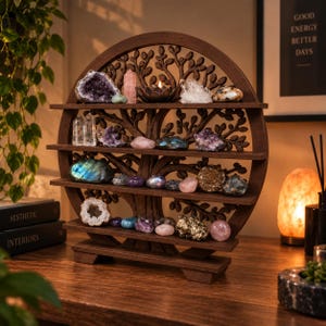 Puede incluir: Un estante de exhibición circular de madera marrón oscura con un intrincado diseño de árbol de la vida y cuatro niveles horizontales. Los estantes están llenos de varios cristales crudos y pulidos, incluyendo amatista, cuarzo y piedras de labradorita.