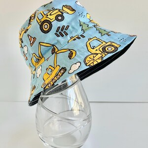 May include: A blue and yellow reversible bucket hat with a construction vehicle print. The hat features a black brim and a yellow construction vehicle design on a light blue background.