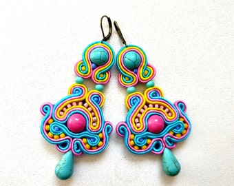 May include: A pair of colorful earrings with a turquoise, pink, and yellow design. The earrings are made of woven thread and have a turquoise stone dangle.