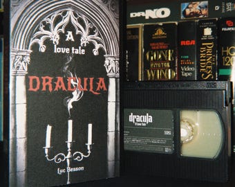 Könnte beinhalten: Eine schwarze VHS-Kassette und die dazugehörige Hülle für den Film Dracula: A Love Tale von Luc Besson. Die Hülle zeigt eine gotische Torbogen-Illustration mit einem Kandelaber und weißem Rauch. Das Kassettenetikett zeigt den Titel und Credits.
