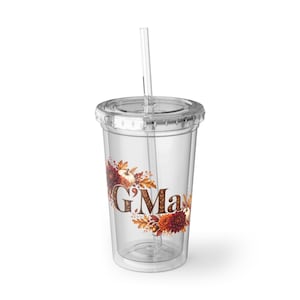 Puede incluir: Un vaso de plástico transparente con tapa y pajita que presenta un gráfico de temática otoñal con hojas, calabazas y flores que rodean el texto G'Ma en una fuente serif marrón. El vaso de doble pared tiene un diseño totalmente transparente.