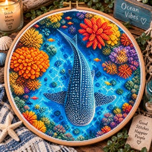 May include: A circular embroidery hoop containing a cross-stitch piece depicting a whale shark swimming through a vibrant coral reef. The scene features a blue ocean background, orange and yellow coral formations, and small orange fish.