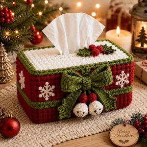 May include: A rectangular crochet tissue box cover in deep red with a white top, decorated with white snowflakes, a large green bow, two small white bells, and red holly berries. The cover features a textured stitch pattern and green trim.
