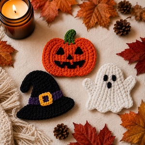 May include: Three crocheted Halloween decorations including an orange jack-o'-lantern with a green stem, a black witch hat with a purple band and yellow buckle, and a white ghost with black eyes and a mouth, all featuring detailed yarn textures.