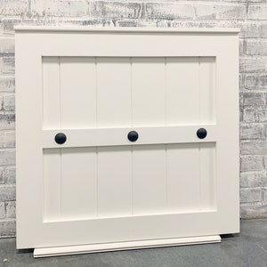 May include: White wooden door with three black knobs. The door has a raised panel design and a small base.