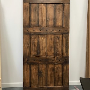 May include: A rustic wooden sliding barn door with a dark brown stain. The door has three horizontal panels with decorative metal accents.