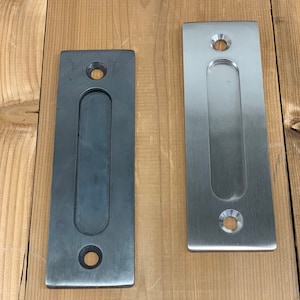 May include: Two rectangular door pulls, one in brushed nickel and one in black, with a recessed handle and two round holes for mounting.