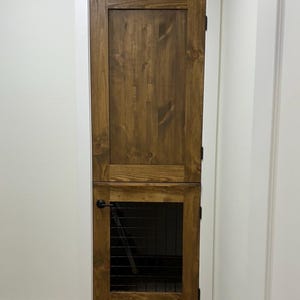 May include: A wooden door with a smaller door below it. The smaller door has a black metal grate. The door is brown and has a black door handle.