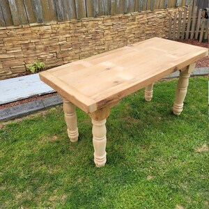 Puede incluir: Una mesa de madera clara con una tapa rectangular y cuatro patas torneadas. La mesa est&aacute; sentada en un c&eacute;sped.