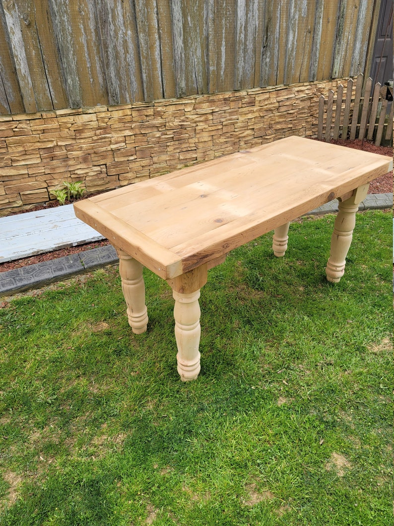 Puede incluir: Una mesa de madera clara con una tapa rectangular y cuatro patas torneadas. La mesa est&aacute; sentada en un c&eacute;sped.