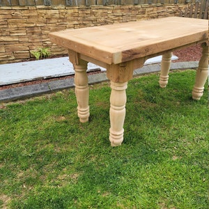 Puede incluir: Una mesa de madera r&uacute;stica con un acabado de madera natural y patas torneadas. La mesa est&aacute; sentada en un c&eacute;sped.